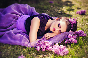 Obraz na płótnie Canvas Beautiful young girl lying in lilac garden