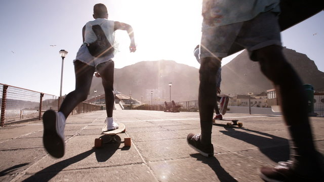African American teenagers longboarding on a walkway at the beach