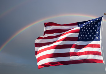 American flag against a cloudy sky with a rainbow - Powered by Adobe