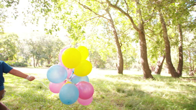 Smiling boy running in park with balloons slow motion
