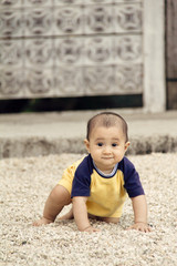 Front view of happy infant crawling on pebble-covered ground