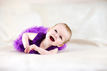 Baby girl in purple dress on white bed