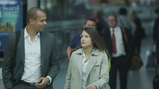 Attractive professional man & woman chat as they walk through busy train station