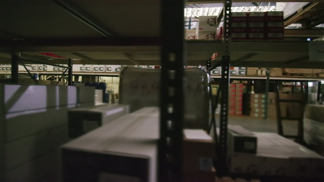Workers in factory or warehouse walking between rows of shelves & checking stock