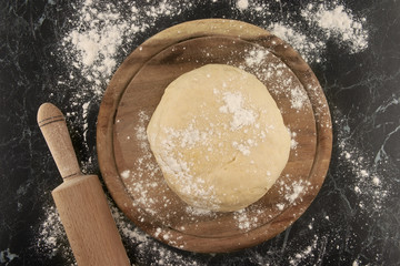 Dough on a wooden board.Rolling pin and flour on table.Top view