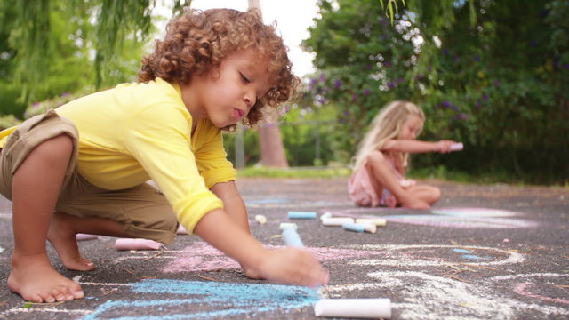 African american boy drawing chalk pictures on a park walkway