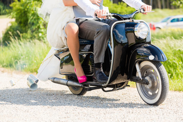 Hochzeitspaar fährt Motorroller in Hochzeitskleid und Anzug