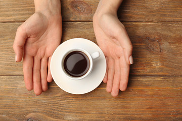 Female hands holding cup of coffee on wooden background