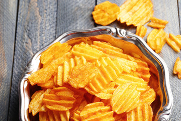 Delicious potato chips on plate on wooden table close-up