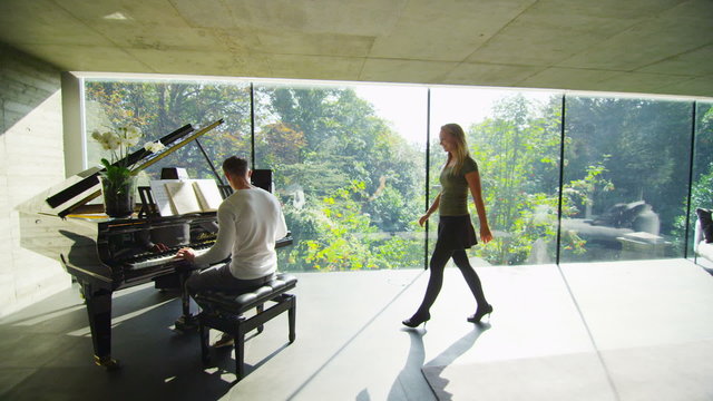 Young man plays the piano in contemporary home as his girlfriend listens