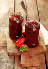 Jars of strawberry jam with berries on wooden background