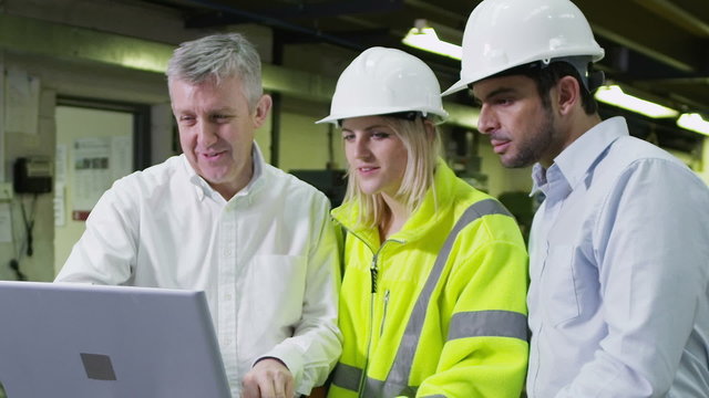 3 workers in a warehouse with a laptop are discussing their work.