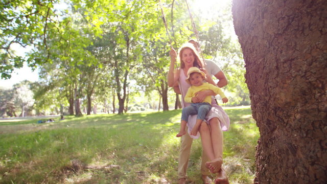 Dad pushing mom and little girl on a swing