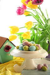 Easter eggs on vase and tulips on table on bright background
