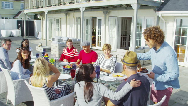 Happy group of family and friends enjoy a meal outdoors at luxury beachside home
