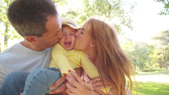 Parents affectionately kissing their little girl on both sides