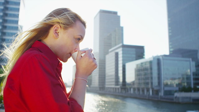Attractive blonde businesswoman drinking coffee as she looks out over city view 