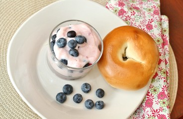 A bowl of yogurt with fresh blueberries and a bagel
