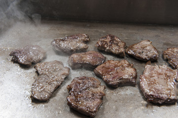 Beef steaks cooking on graill at at restaurant buffet