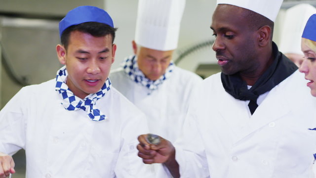 Chef cooking in commercial kitchen waits for head chef to taste & give approval