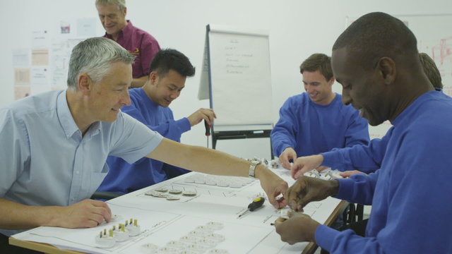 Happy male factory staff of mixed ethnicity assembling electrical fittings