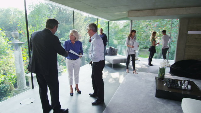 Mature couple talking to estate agent at open viewing of luxury modern home