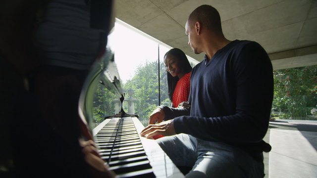 Young man and his love sit down to play the piano together
