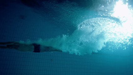 Underwater view of a professional male swimmer diving into deep blue water