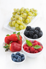 Fresh garden berries and grapes on white wooden table, vertical