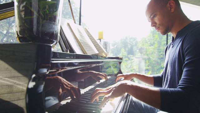 Young man plays the piano alone in contemporary home with sunlight streaming in
