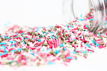 Spilled sprinkles with container on white background