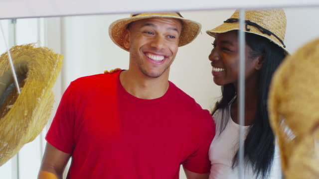 Young happy couple have fun trying on a selection of straw hats.