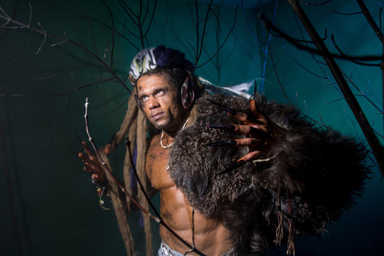 Muscular man with dreadlocks and skin through the trees.