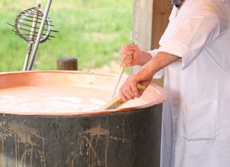 cheesemaker checks the temperature of the boiling milk in the po