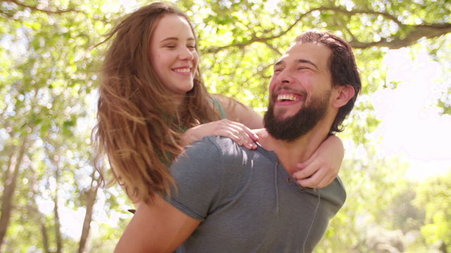Guy piggybacking his laughing girlfriend in a sunny park