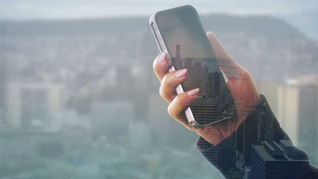 Hands using a touch screen phone with city visual background