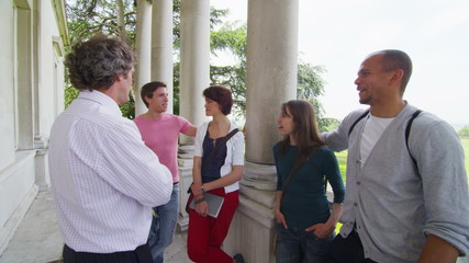 Happy group of students chatting with their teacher outside college building 