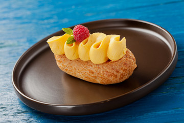 Single eclair with cream and raspberry on plate.