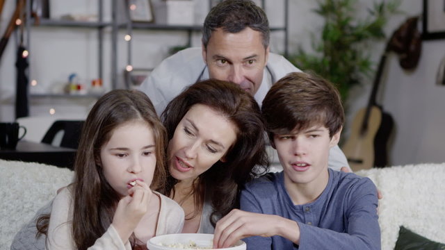 Happy family watching t.v. together and eating popcorn