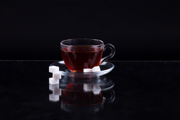 cup of black tea with slices of sugar on a black background