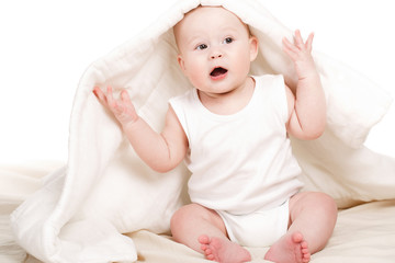 Cute baby peeking out from under the blanket,playing on the bed.
