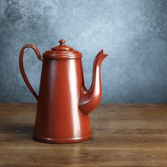 Red retro coffee pot on wooden table behind grey wall