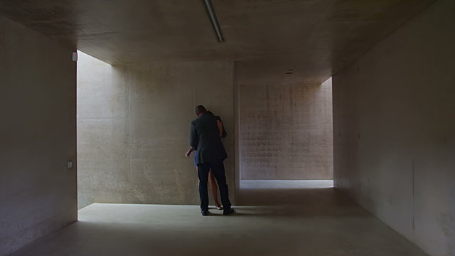 Sexy young couple walking through modern concrete building stop to share a kiss