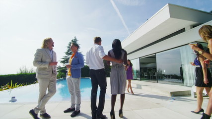 Glamorous friends enjoying drinks by the pool outside luxury modern home
