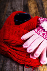 Cup of hot drink wrapped by red scarf and gloves on wooden board