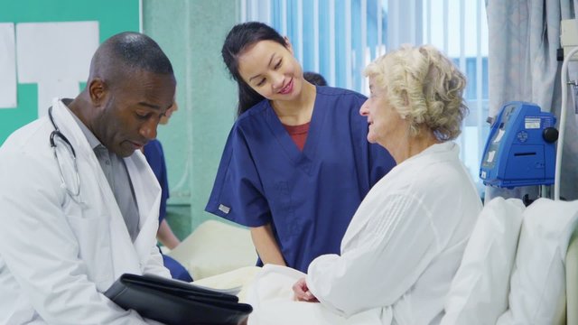 Caring Doctor And Nurse Chatting With An Elderly Female Patient At Her Bedside