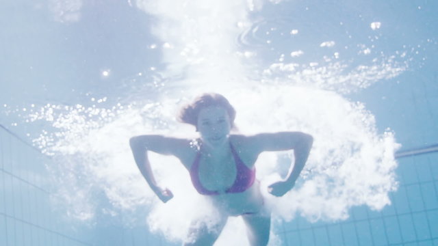 Beautiful woman in a pink bikini diving in and swimming underwater