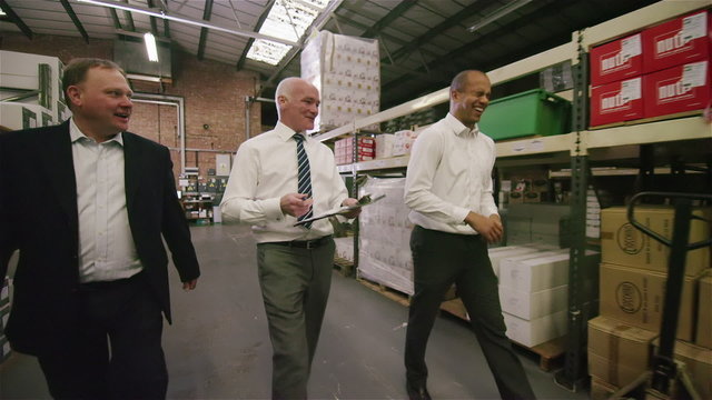 Workers in factory or warehouse walking between rows of shelves & checking stock