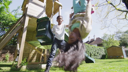 Cute young brother and sister playing on the swings on a hazy summer day