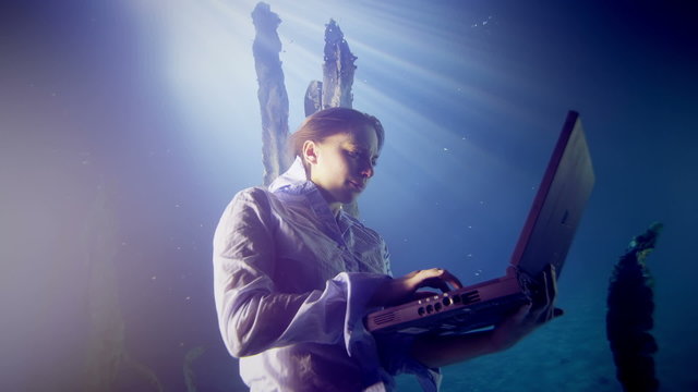 Underwater businesswoman working on a laptop computer in deep blue water